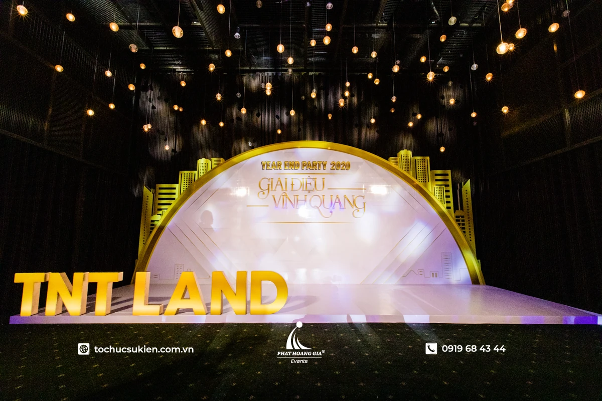 Backdrop tiệc tất niên và gala công ty với thiết kế tông vàng ấm, ánh đèn trang trí và chủ đề Year End Party