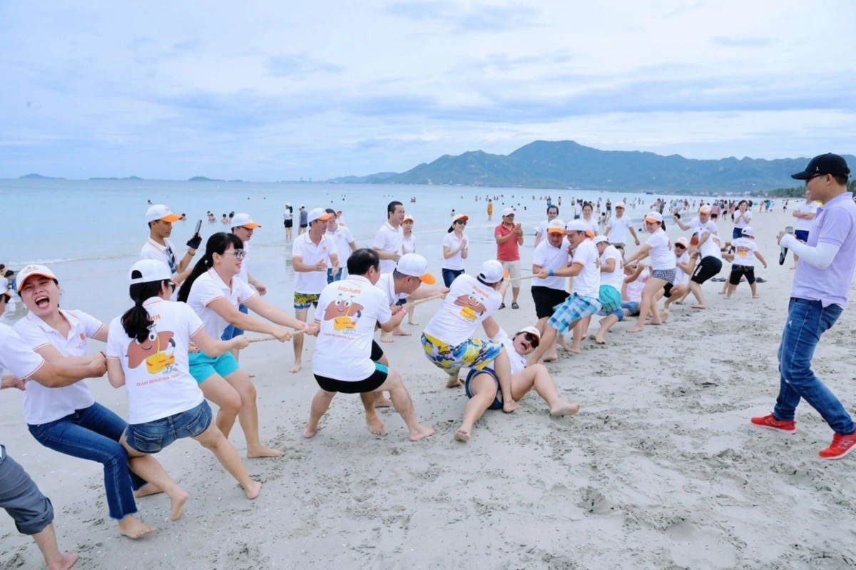 MC dẫn dắt và các đội nhân viên cổ vũ trong trò chơi kéo co team building ngoài trời