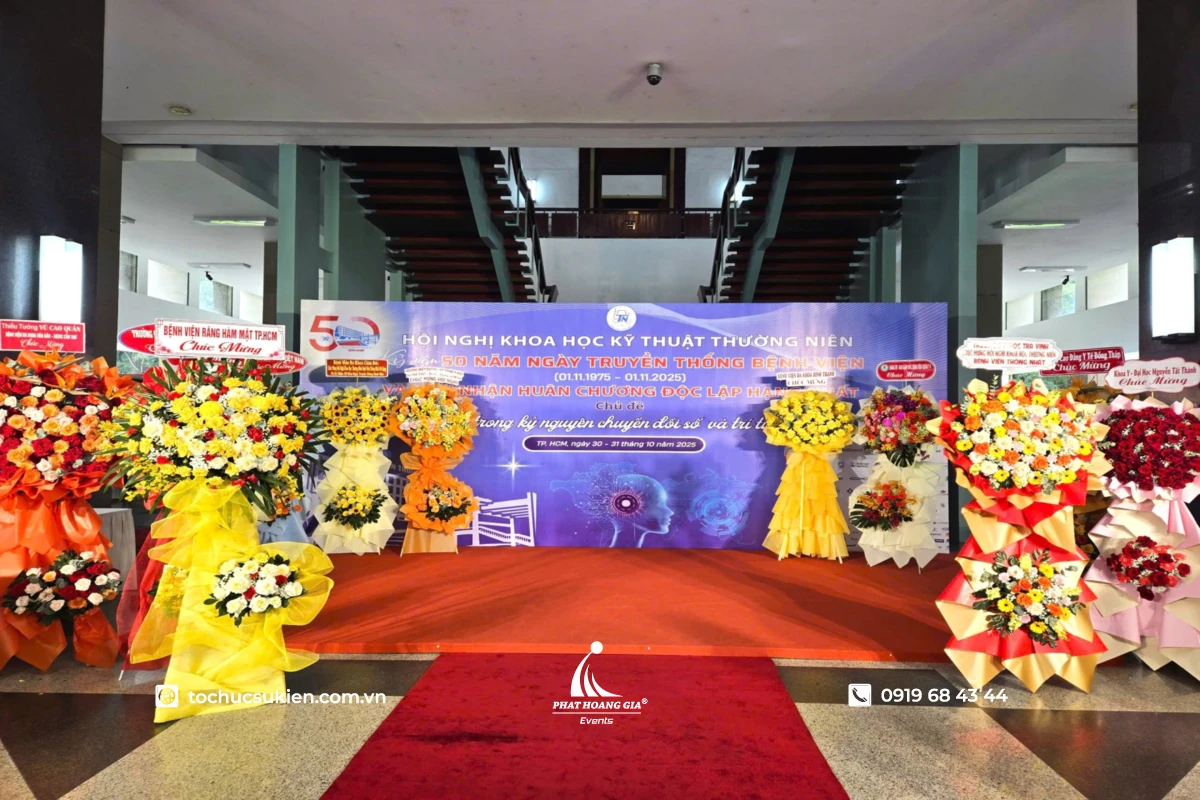 Backdrop check-in hội nghị khoa học kỹ thuật thường niên với thảm đỏ và khu vực hoa chúc mừng tại sảnh sự kiện