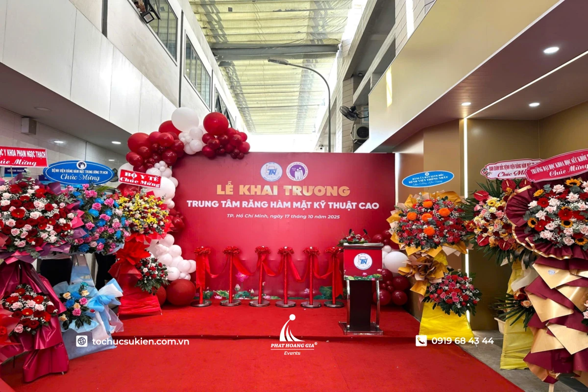 Trang trí lễ khai trương trung tâm với backdrop đỏ, khu vực cắt băng khánh thành và hoa chúc mừng hai bên