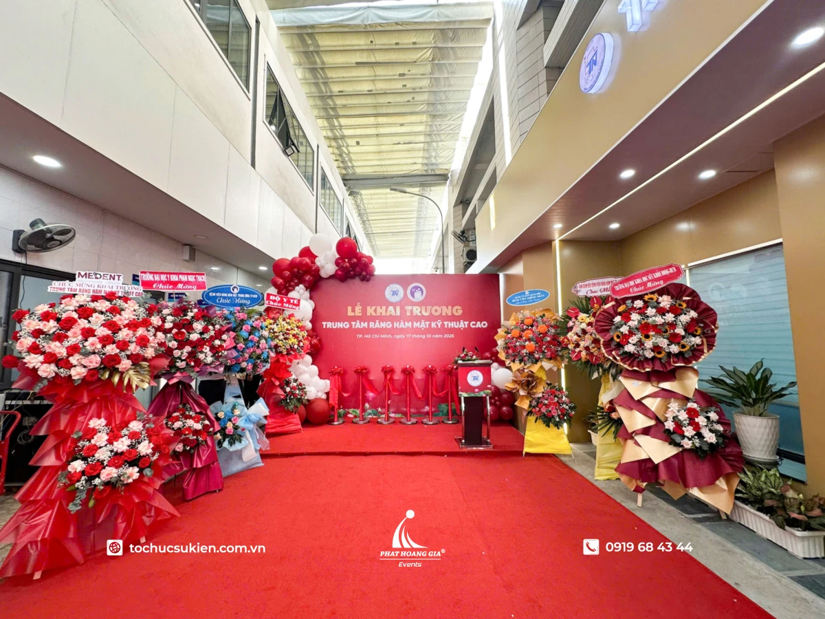 Kệ hoa và lẵng hoa được bố trí sắp xếp xung quanh trước backdrop sân khấu  khai trương doanh nghiệp 