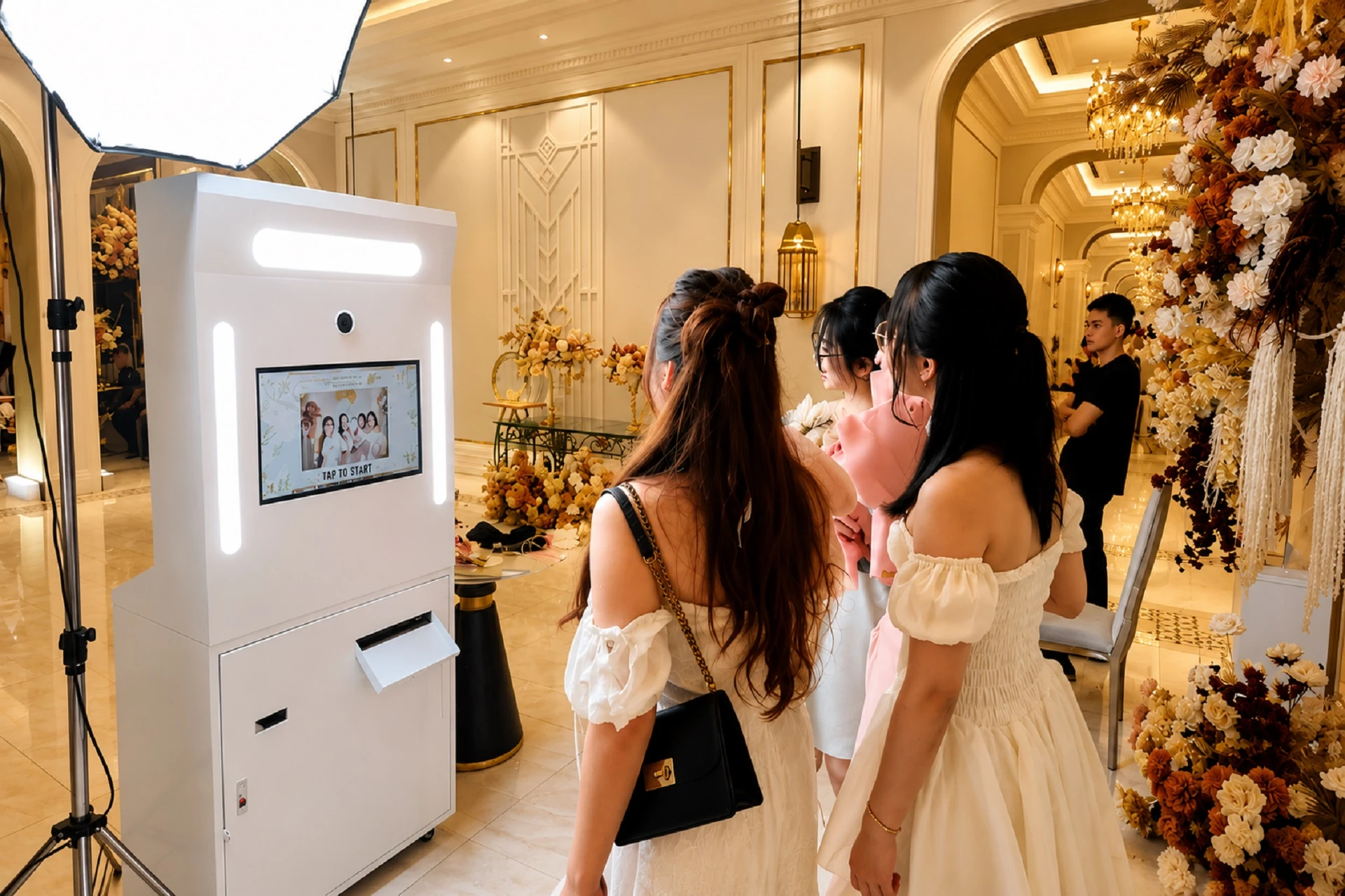 Khu vực photobooth sự kiện trong sảnh khách sạn với máy chụp ảnh tự động, đèn studio và khách mời trải nghiệm chụp ảnh
