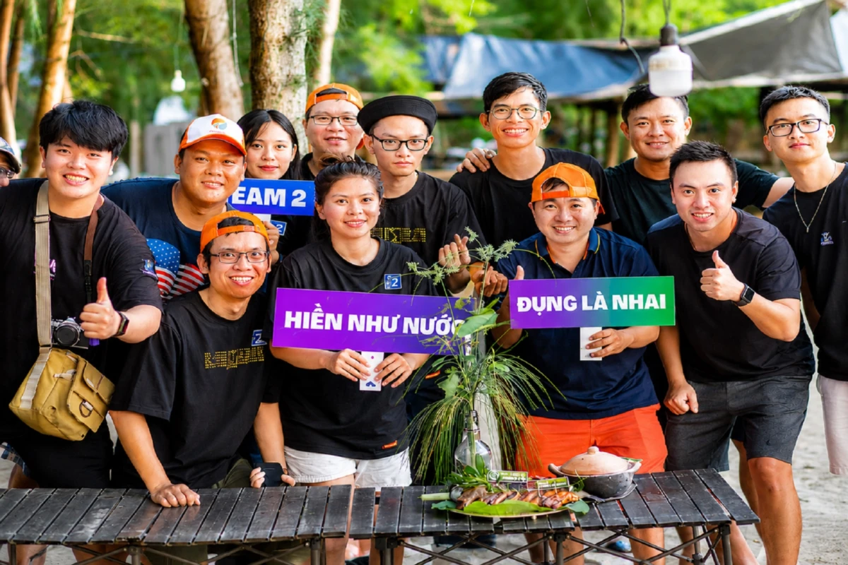 Nhóm nhân viên team building cầm bảng slogan hài hước, thể hiện tinh thần đoàn kết