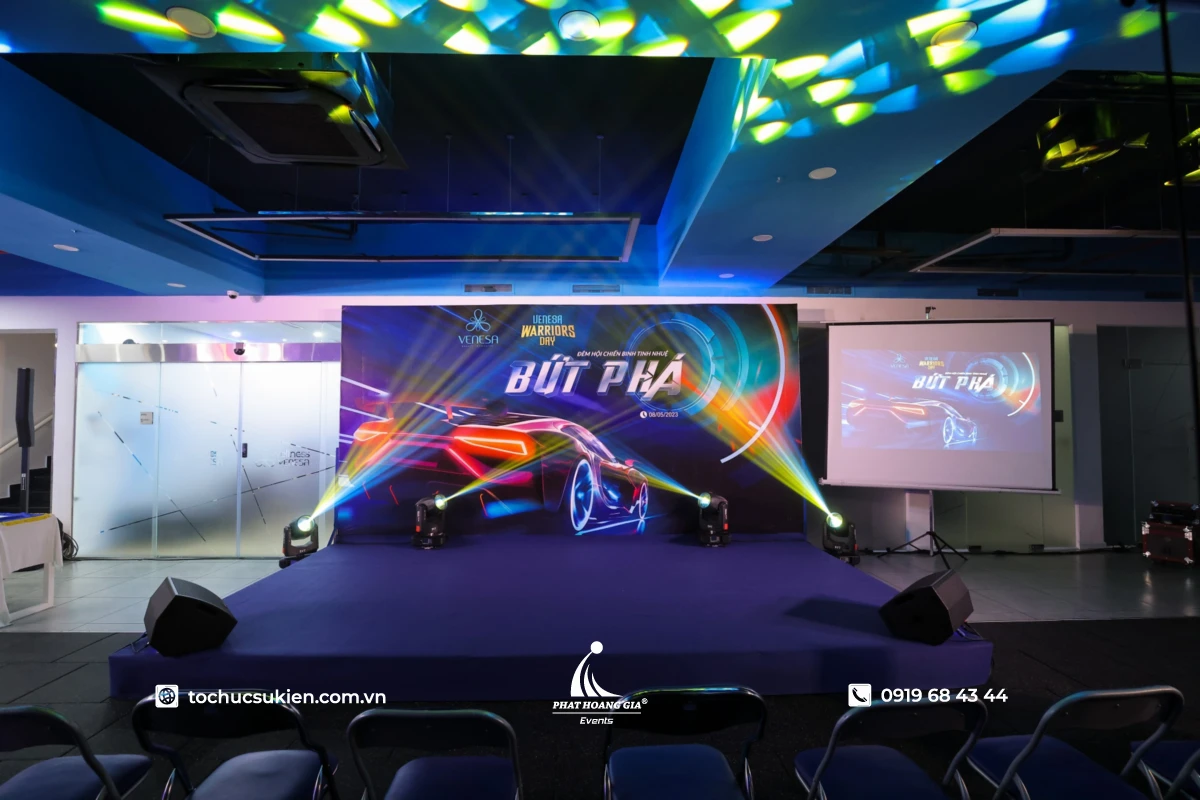 Không gian event công ty theme bứt phá với sân khấu tím, backdrop xe thể thao neon và ánh sáng nổi bật