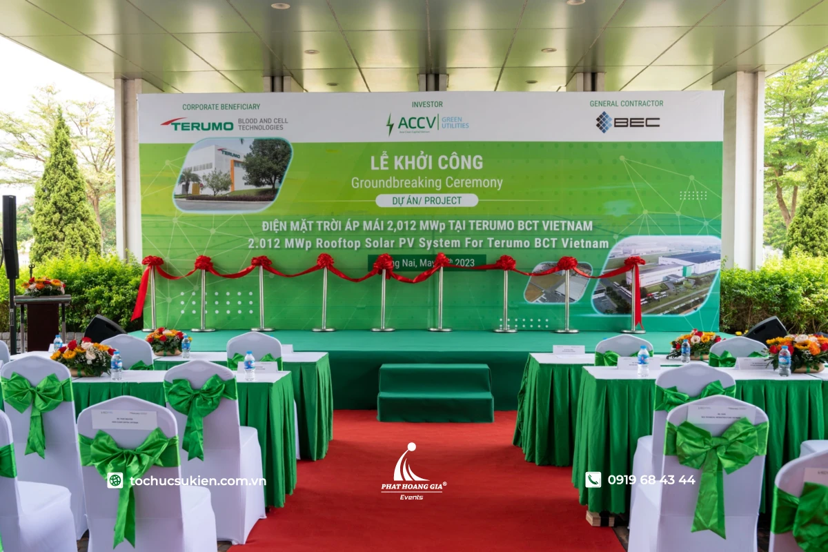 Sân khấu lễ khởi công doanh nghiệp với backdrop, khu vực cắt băng khánh thành và không gian sự kiện ngoài trời