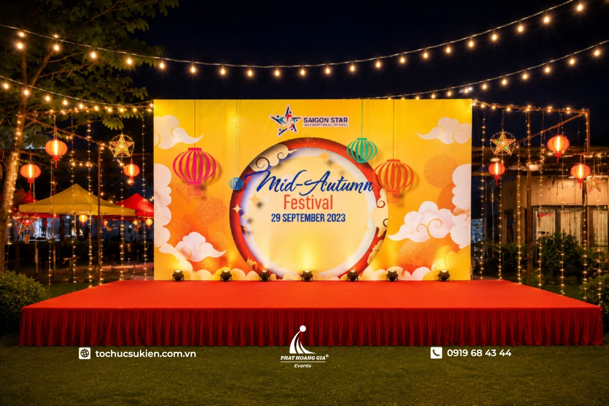 Sân khấu Trung Thu ngoài trời với backdrop trăng rằm, đèn lồng truyền thống và hệ thống dây đèn trang trí lung linh vào buổi tối