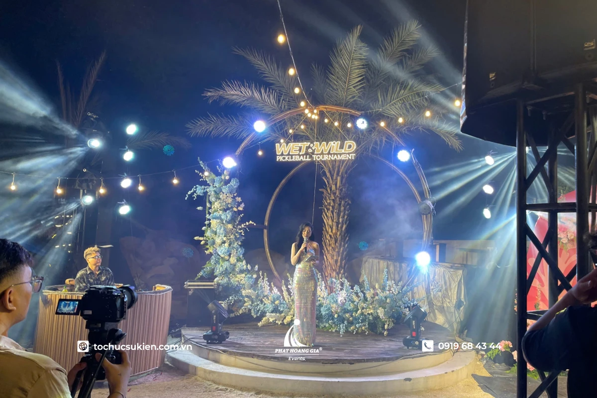 Nữ MC duyên dáng dẫn chương trình trên sân khấu với thiết kế background gala dinner ngoài trời độc đáo