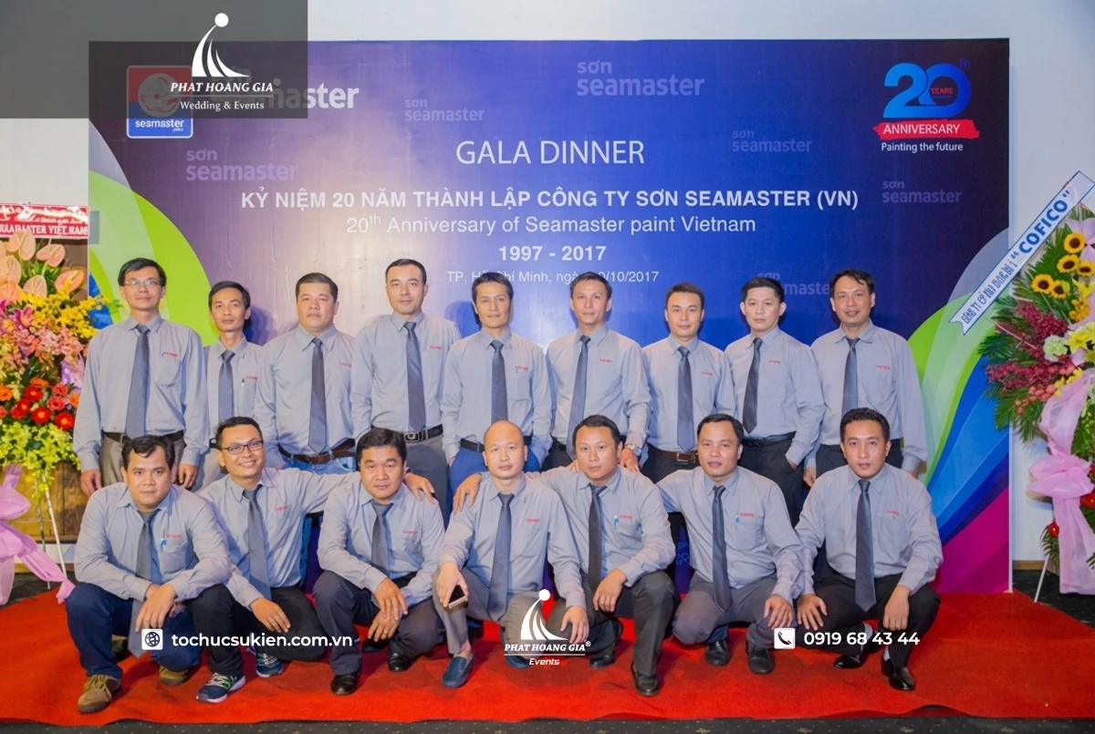 Đội ngũ nhân sự đứng check in trên thảm đỏ trước backdrop kỷ niệm gala dinner công ty