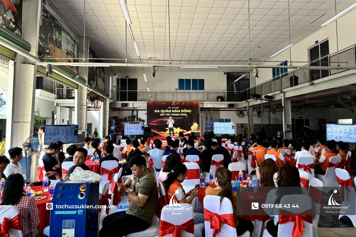 Toàn cảnh year end party doanh nghiệp với nhân viên ngồi bàn tròn và lãnh đạo phát biểu trên sân khấu