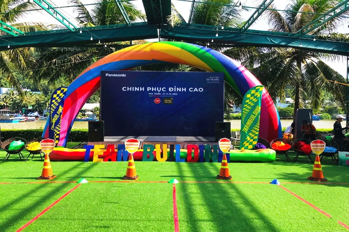 Backdrop team building sân khấu ngoài trời với cổng hơi cầu vồng nổi bật.