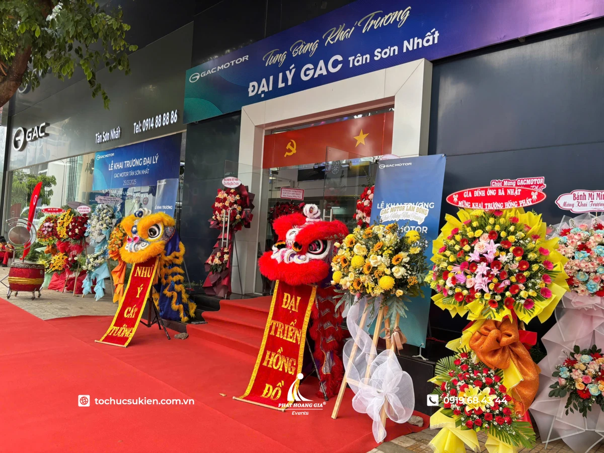 Banner khai trương treo trước đại lý GAC Tân Sơn Nhất trong không gian chúc mừng đầy hoa và đội lân đón khách.