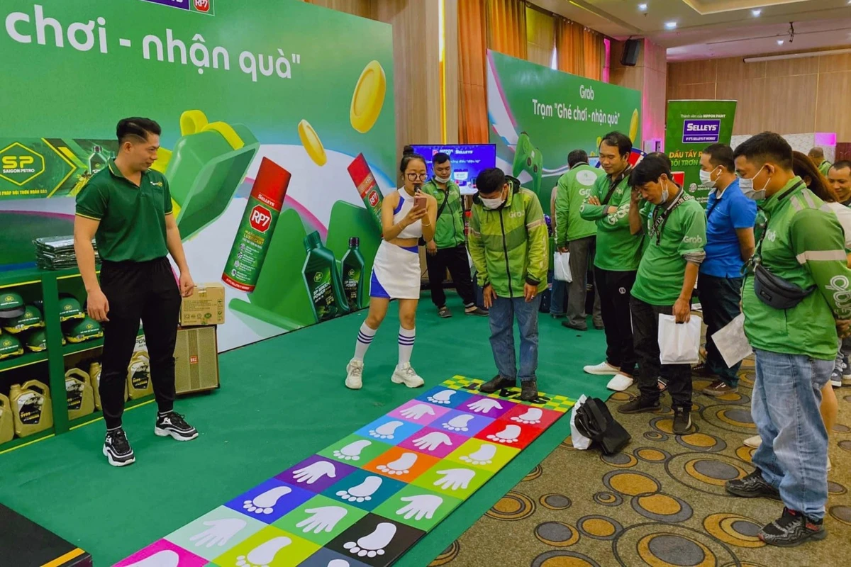 PG đang tương tác và hướng dẫn khách hàng tham gia hoạt động tại booth quảng cáo sản phẩm để nhận quà tặng trong không gian sự kiện thương hiệu