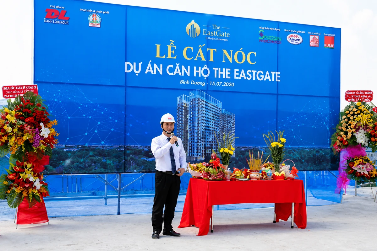 Lễ cất nóc dự án chung cư với sân khấu ngoài trời ban giám đốc đứng phát biểu và mâm cúng lễ bên cạnh