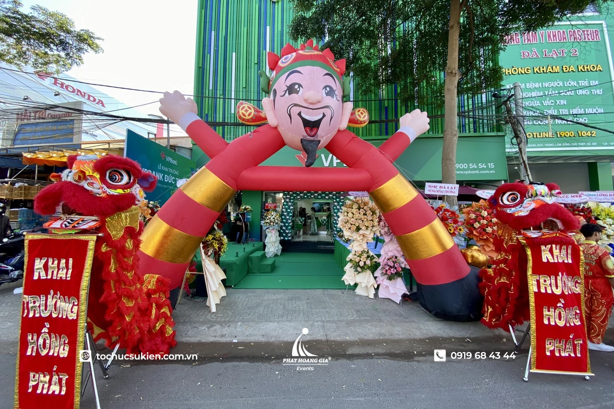 Cổng chào sự kiện khai trương với mô hình Thần Tài inflatable nổi bật phía trước, kết hợp múa lân đón khách tạo không khí sôi động, thu hút