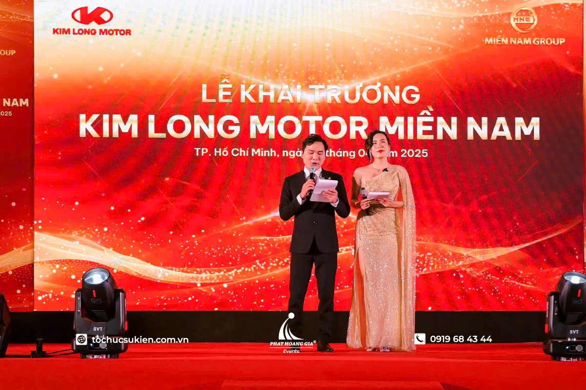 MC đứng trên sân khấu với không gian sự kiện được đầu tư hoành tráng, chuyên nghiệp cùng hệ thống ánh sáng và màn hình hiện đại