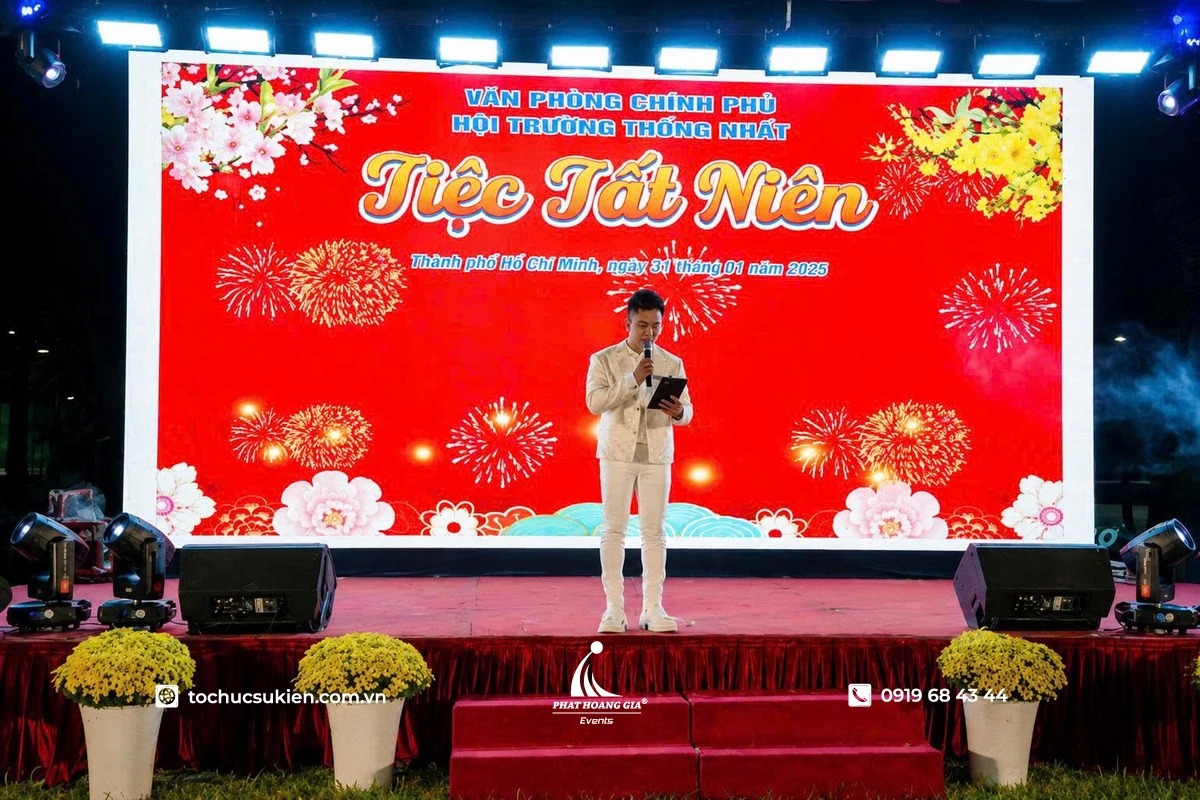 Nam MC cầm kịch bản dẫn chương trình trên sân khấu tiệc tất niên tone đỏ nổi bật với không gian chuyên nghiệp và sang trọng