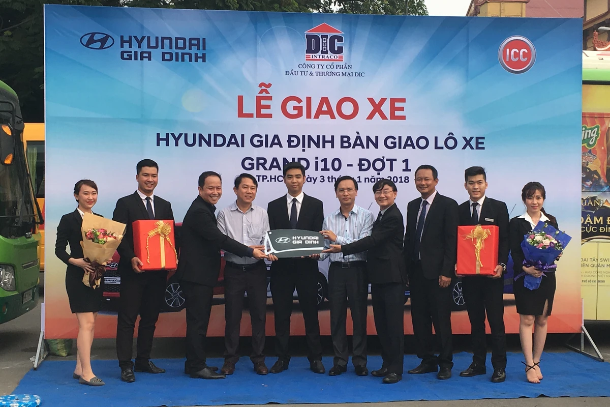 Nhóm khách hàng nhận xe và trao chìa khóa tại lễ bàn giao xe với backdrop và logo thương hiệu phía sau