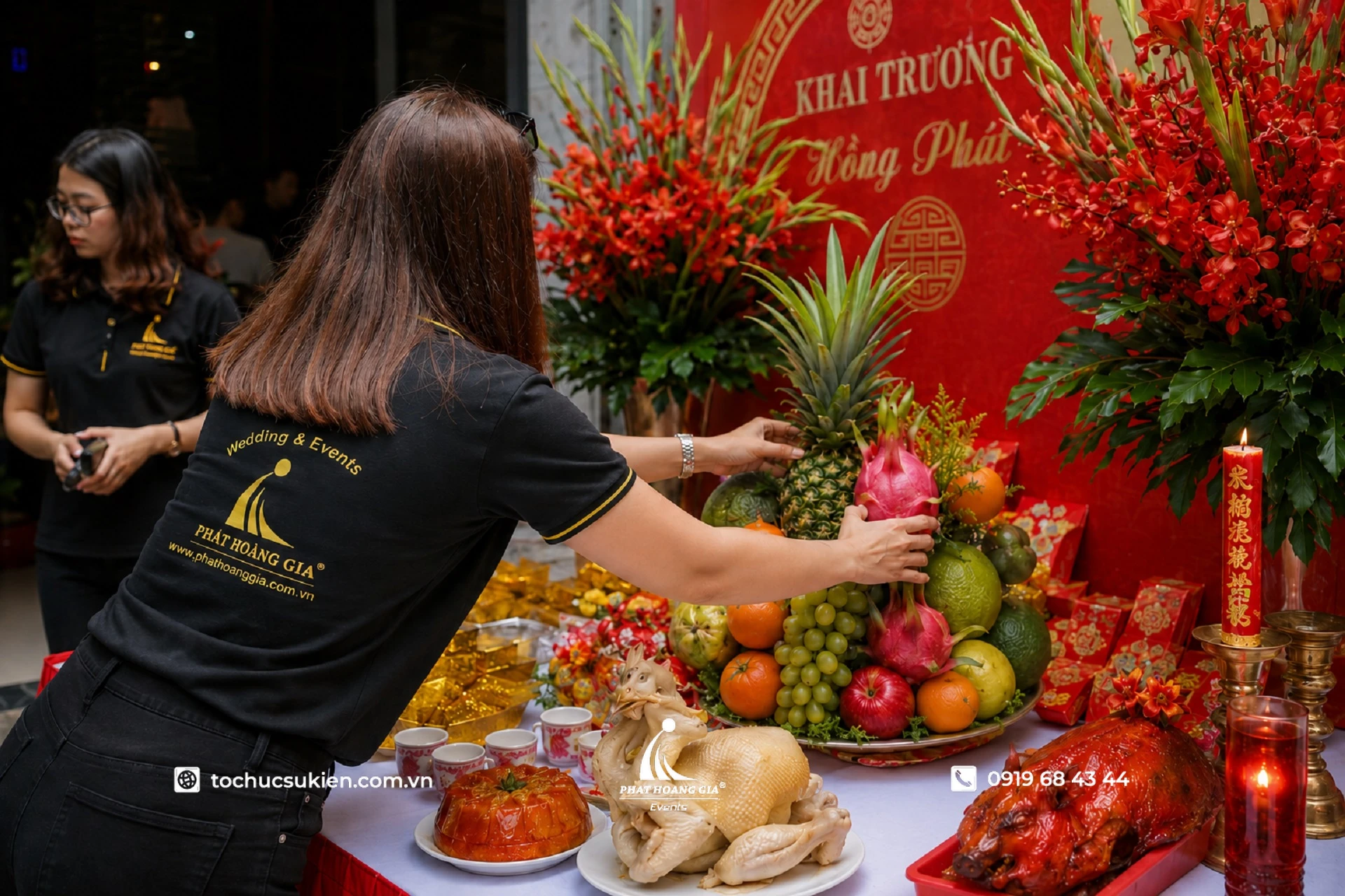 Nhân viên sự kiện đang sắp xếp mâm ngũ quả và lễ vật cúng khai trương trên bàn cúng trước giờ làm lễ