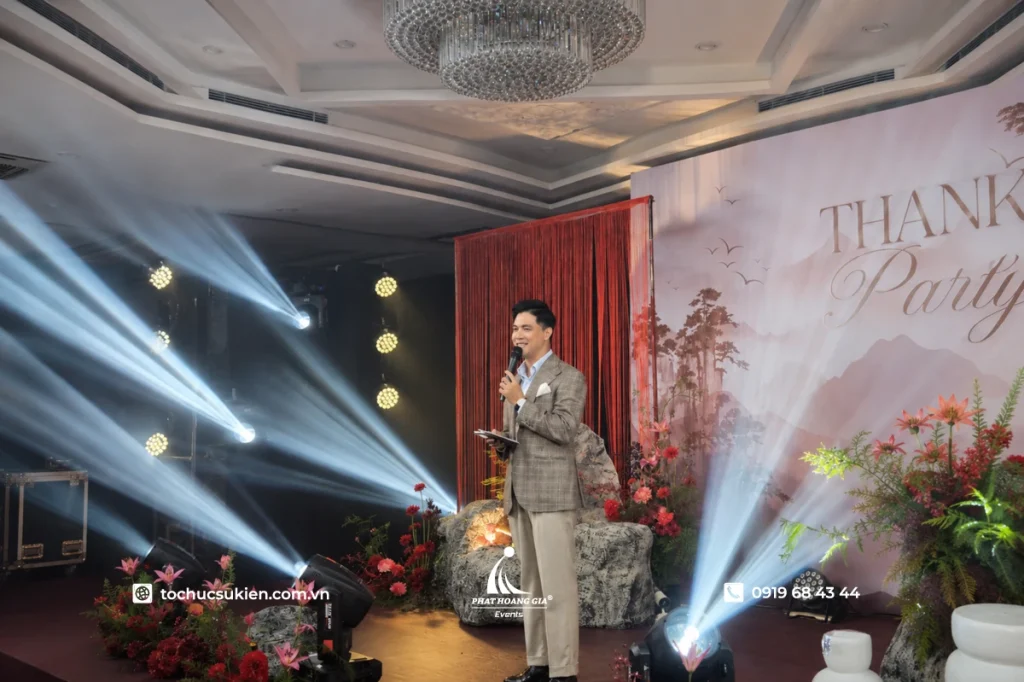 Nam mc mặc vest caro lịch lãm dẫn dắt bữa tiệc thank you party dưới ánh đèn sân khấu chuyên nghiệp.