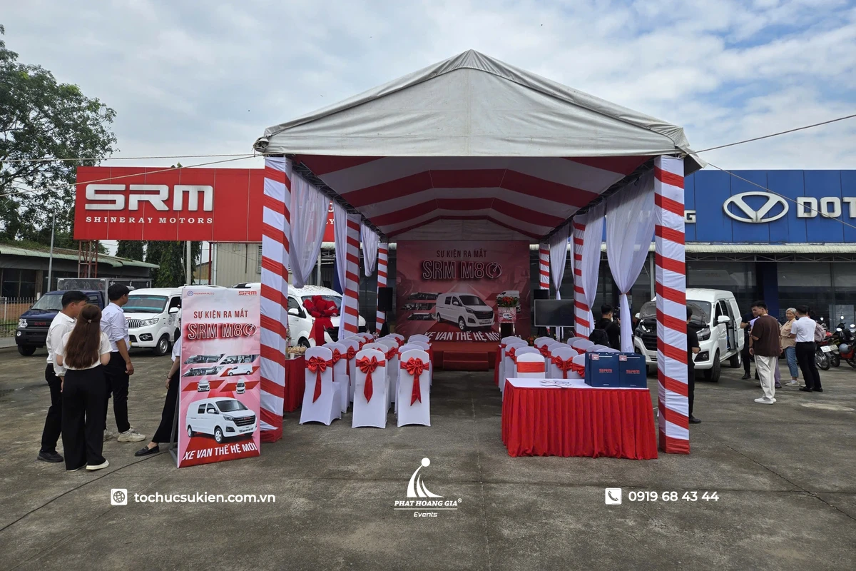 Nhà bạt không gian mái trắng được dựng ngoài trời cho sự kiện ra mắt xe SRM M80, trang trí tông đỏ trắng với sân khấu, bàn ghế phủ nơ và khu vực đón khách chuyên nghiệp