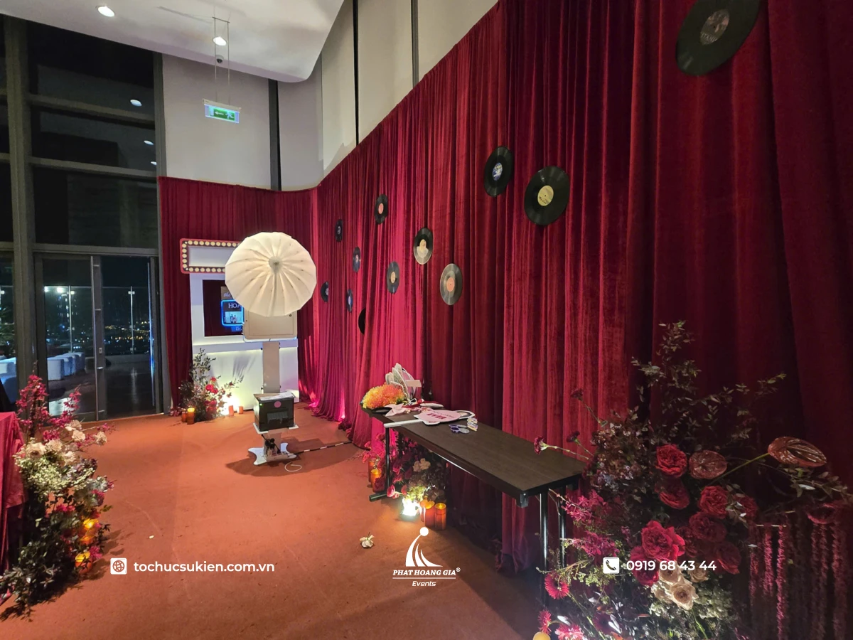 Ekip thi công photo booth tại sự kiện với khung trang trí backdrop logo và hashtag đặt sẵn trên bàn.