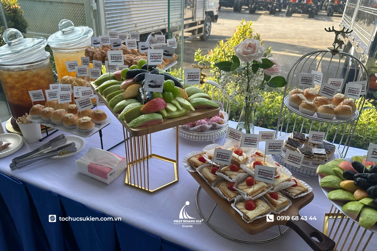 Bàn tea break menu được bố trí đẹp mắt với đa dạng bánh ngọt, trái cây tươi, nước uống và dụng cụ phục vụ sắp xếp gọn gàng trong không gian sự kiện