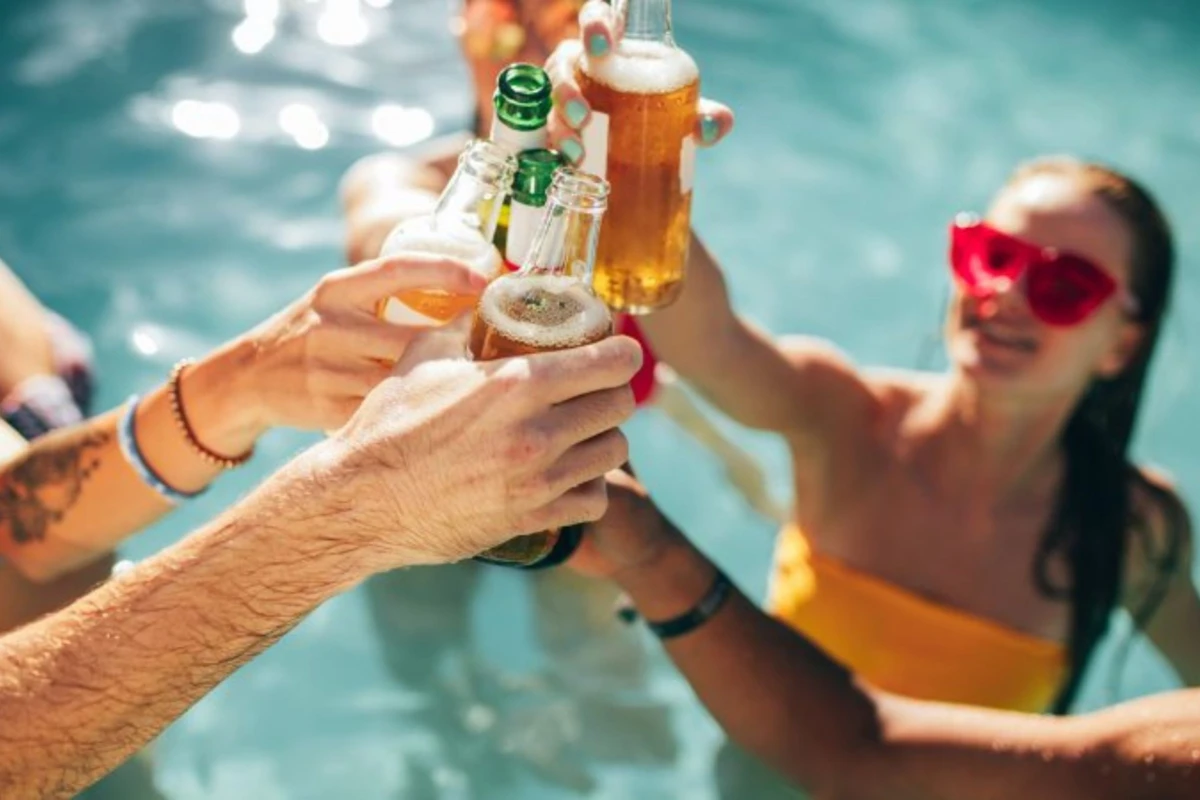 Nhóm bạn trẻ cùng nâng bia và ly cocktail tận hưởng tiệc bể bơi.