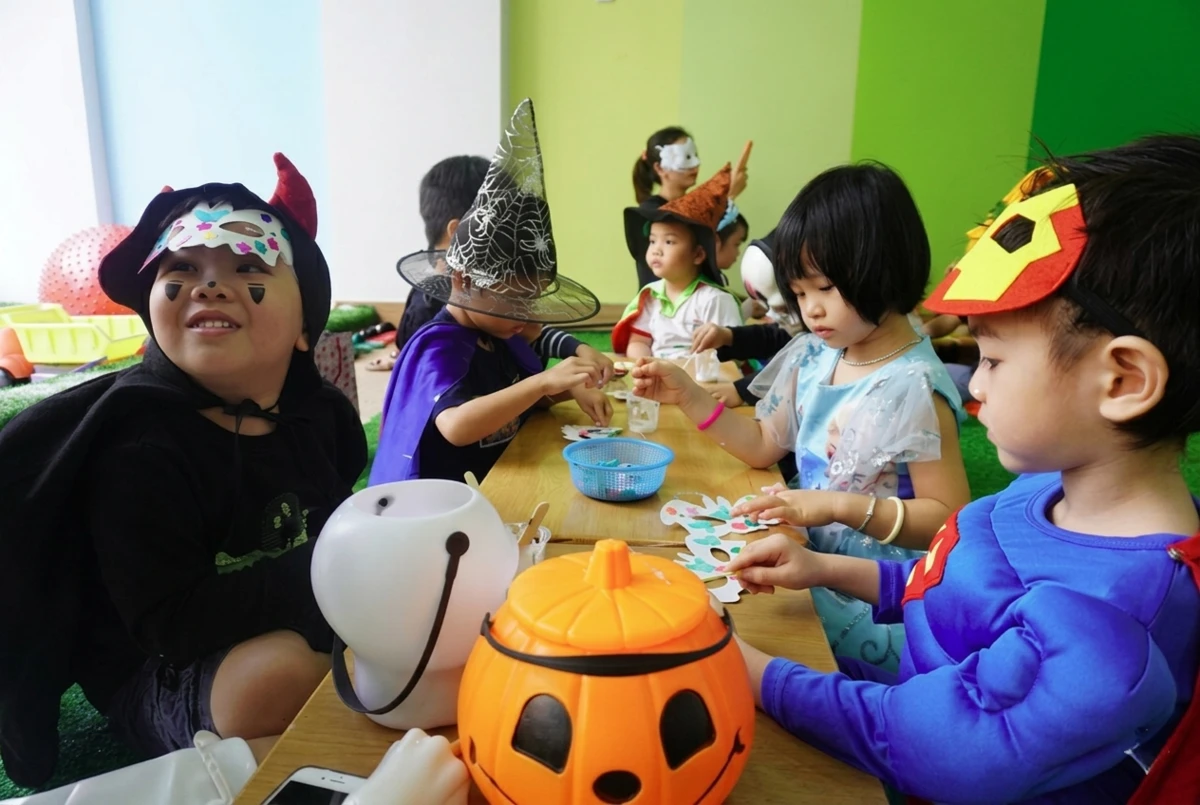 Các bạn nhỏ mầm non hào hứng ngồi làm mặt nạ giấy thủ công và trang trí bí ngô khi trường tổ chức halloween