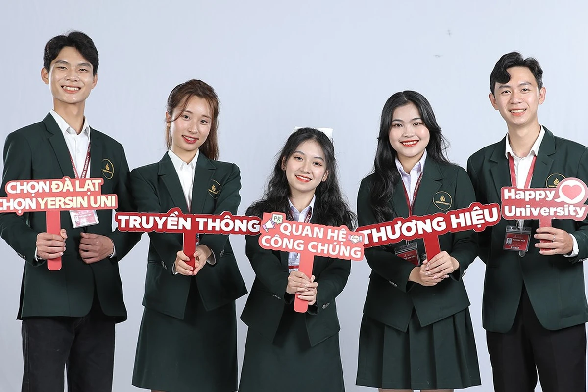 Nhóm sinh viên trường Đại học Yersin Đà Lạt mặc đồng phục vest xanh cầm bảng hashtag truyền thông ngành Quan hệ công chúng