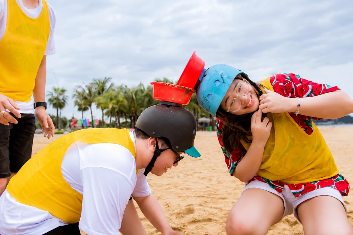 Các thành viên tham gia trò chơi chuyền nước bằng xô đội đầu trong chương trình team building trên bãi biển, mang đến không khí vui nhộn và đầy thử thách