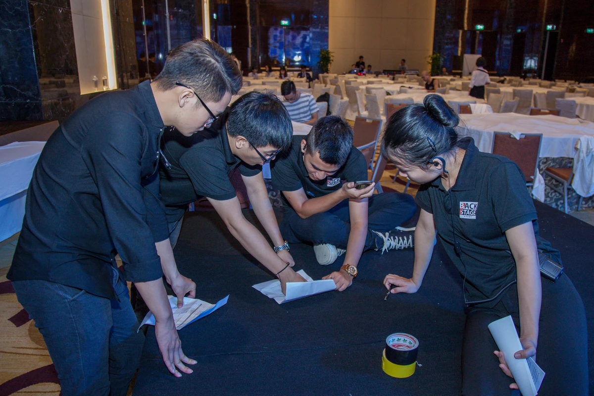 Event Manager đang phổ biến kế hoạch triển khai, phân công nhiệm vụ và lưu ý vận hành cho các thực tập sinh trước khi chương trình diễn ra